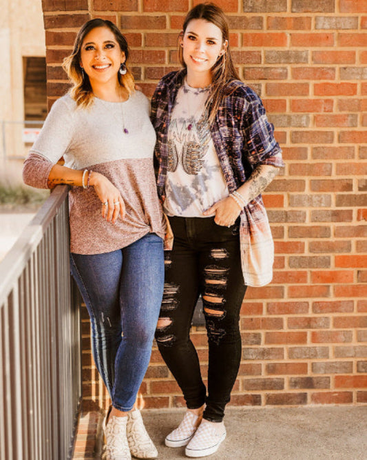 Two women standing on a balcony with a brick wall background